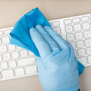 a hand wiping keyboard wearing blue disposable gloves.