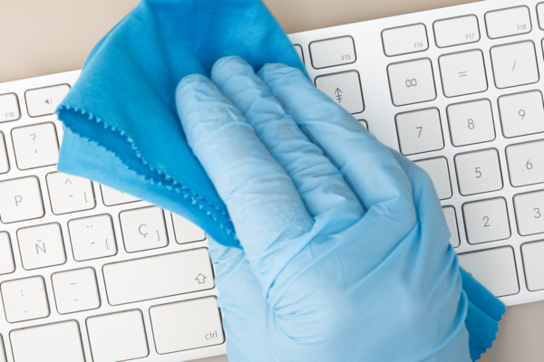 a hand wiping keyboard wearing blue disposable gloves.