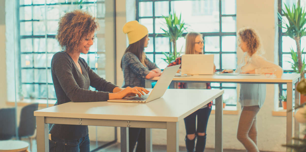 Four young women using standing desks at the office.