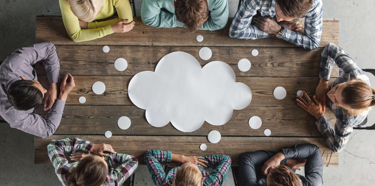 Coworkers gathered around a paper thought bubble on a table.