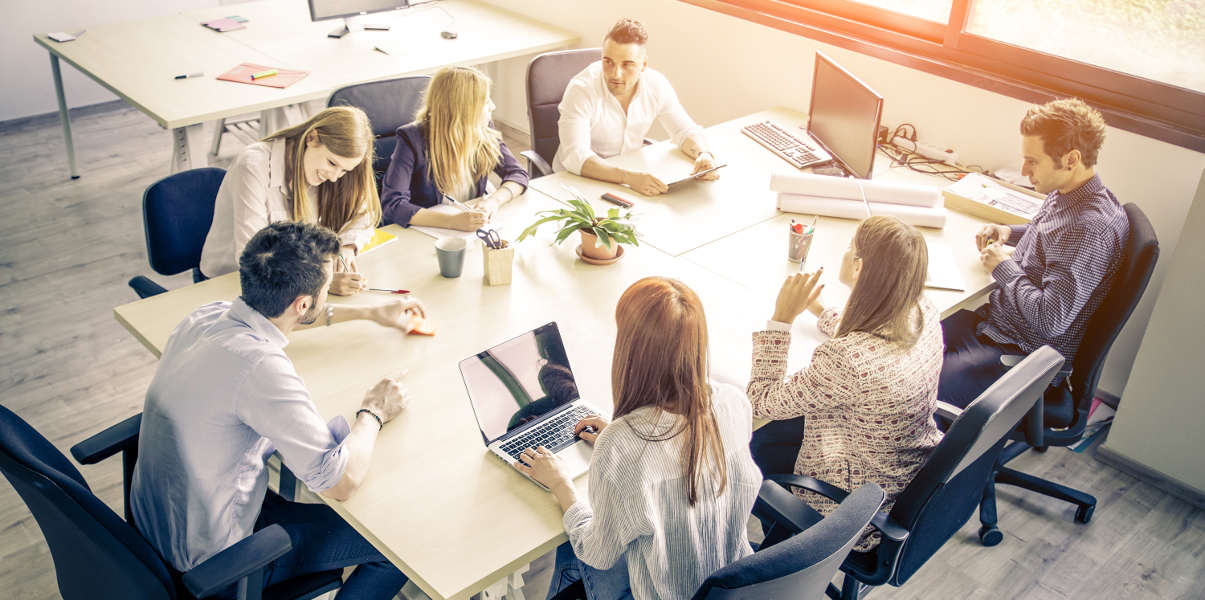 Young professionals gathered around a large wooden conference table.