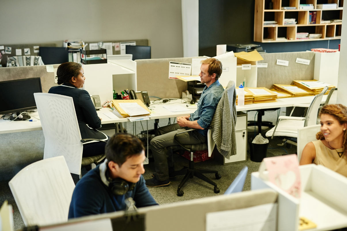 Two co-workers collaborating in their cubicles at the office.